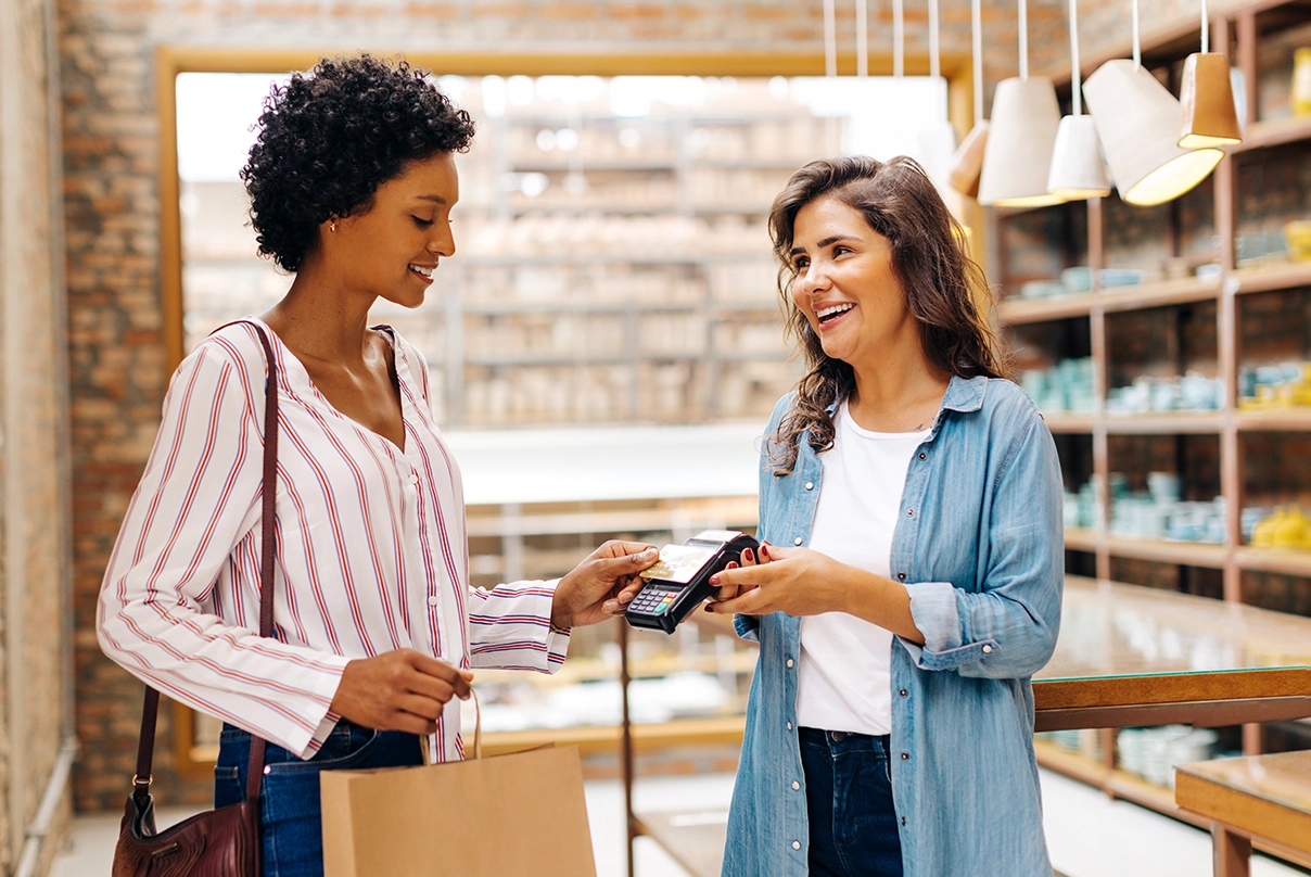 Risparmiare soldi con budgeting: Donna afro americana effettua pagamento in un negozio fisico alla commessa