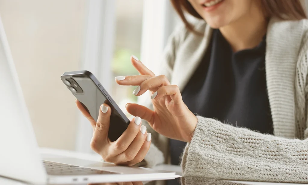 Donna che utilizza lo smartphone per effettuare pagamenti digitali online mentre lavora al computer