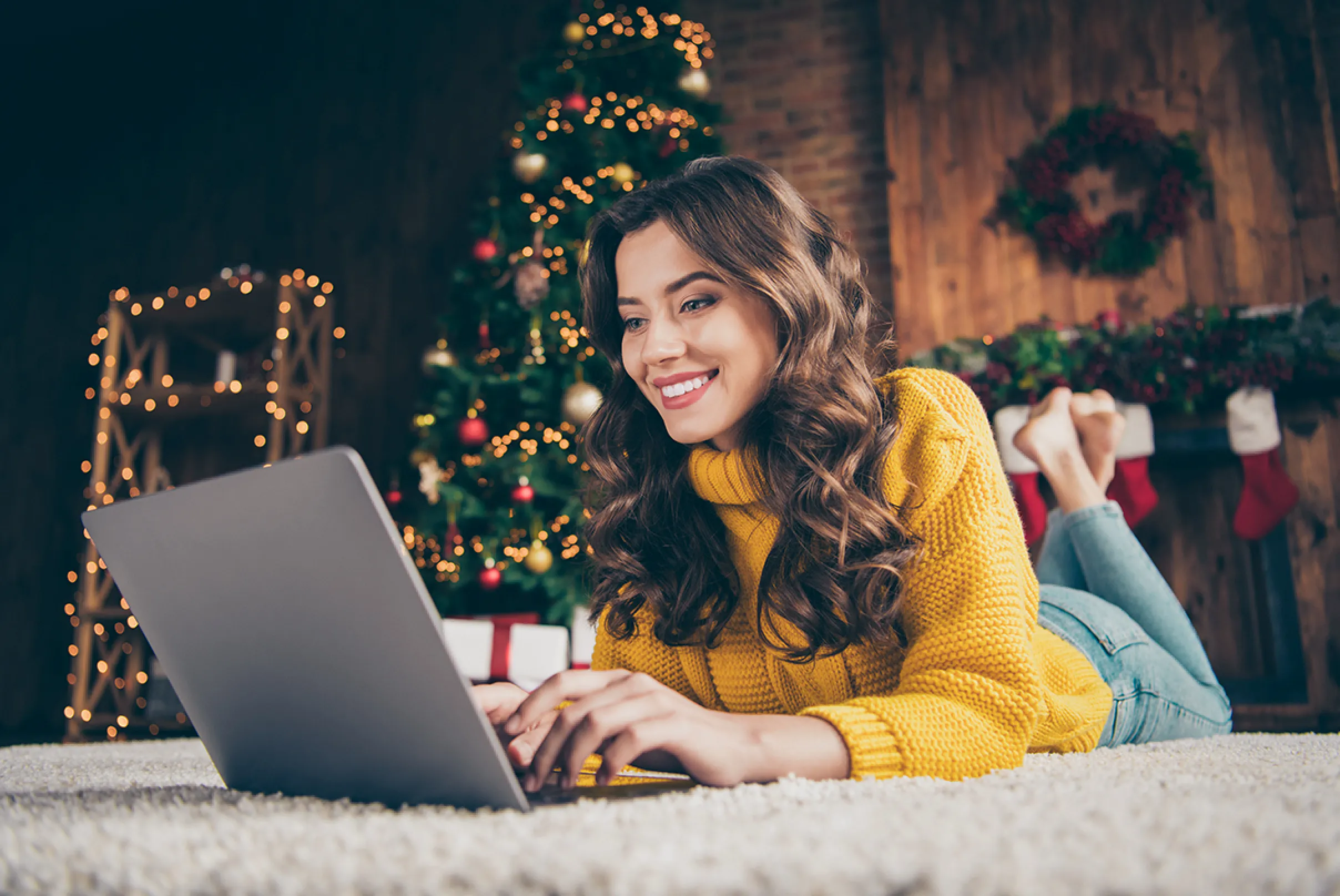 Donna che acquista online i regali di Natale dal laptop in un ambiente decorato a festa, simbolo dello shopping natalizio digitale.