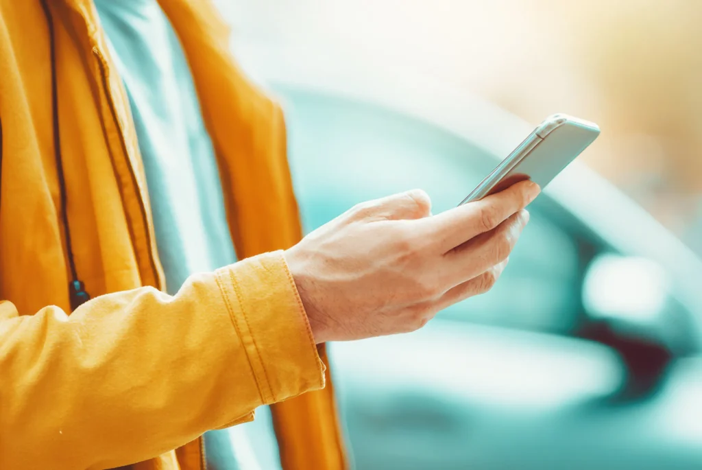 Persona che utilizza lo smartphone per pagare il bollo auto online, con l’auto sullo sfondo, simbolo dei servizi digitali di pagamento.